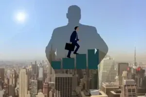 The business-man-6583632_640 image shows a businessman climbing bar graph steps with a city skyline behind him. In the background, theres a shadow of a bigger figure, which stands for ambition and growth beneath a bright sun. Subscribe For a Free eBook