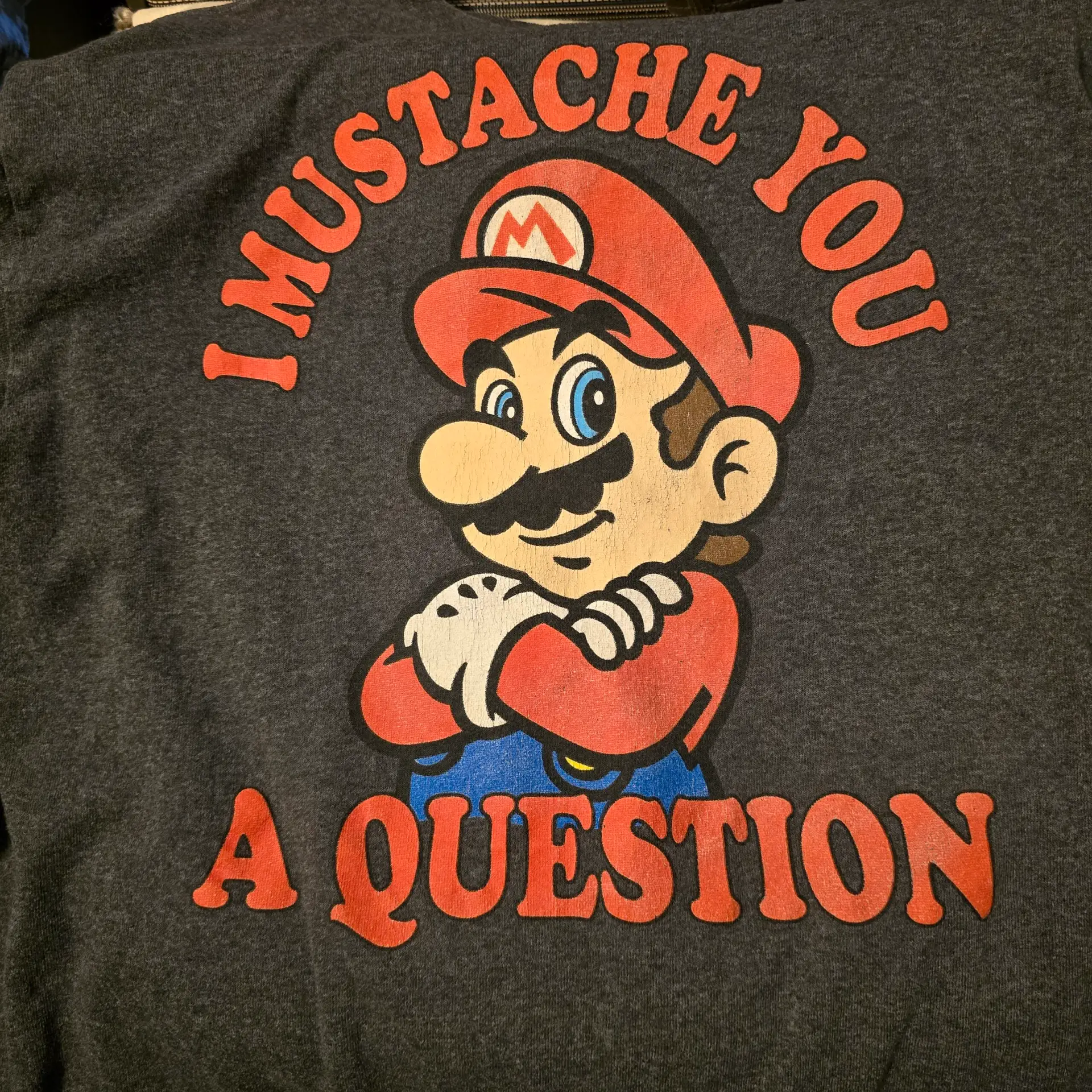 What Are Some of The Dangers of Having Low Testosterone Levels Cartoon with a red-hat, mustached character, arms crossed, saying I MUSTACHE YOU A QUESTION in big red letters.